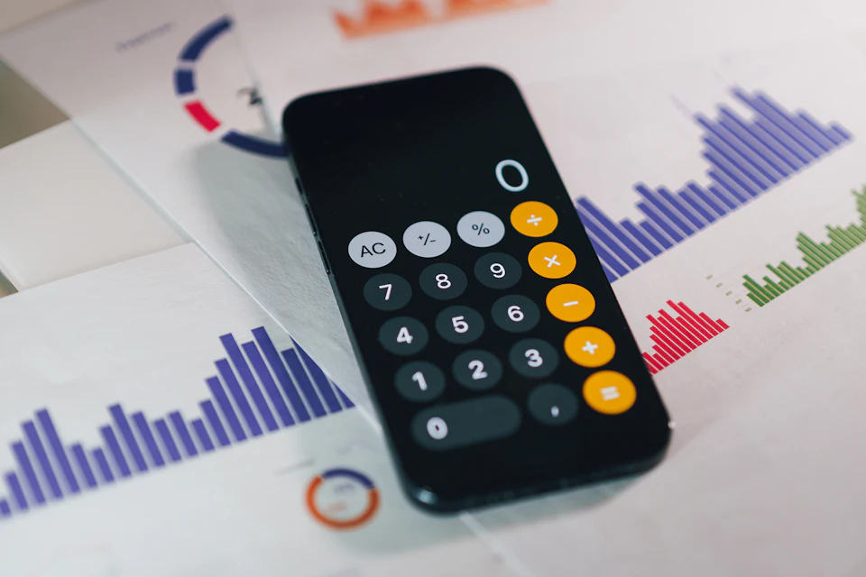 Taschenrechner auf Smartphone-Display über Diagrammen und Unterlagen
