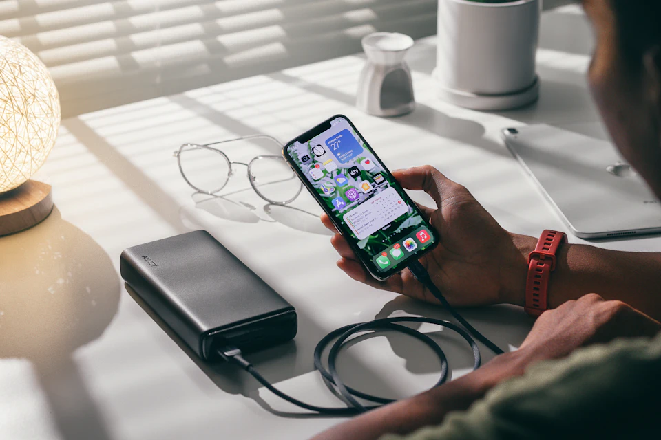Smartphone wird über eine Powerbank mit Kabel auf einem Tisch geladen